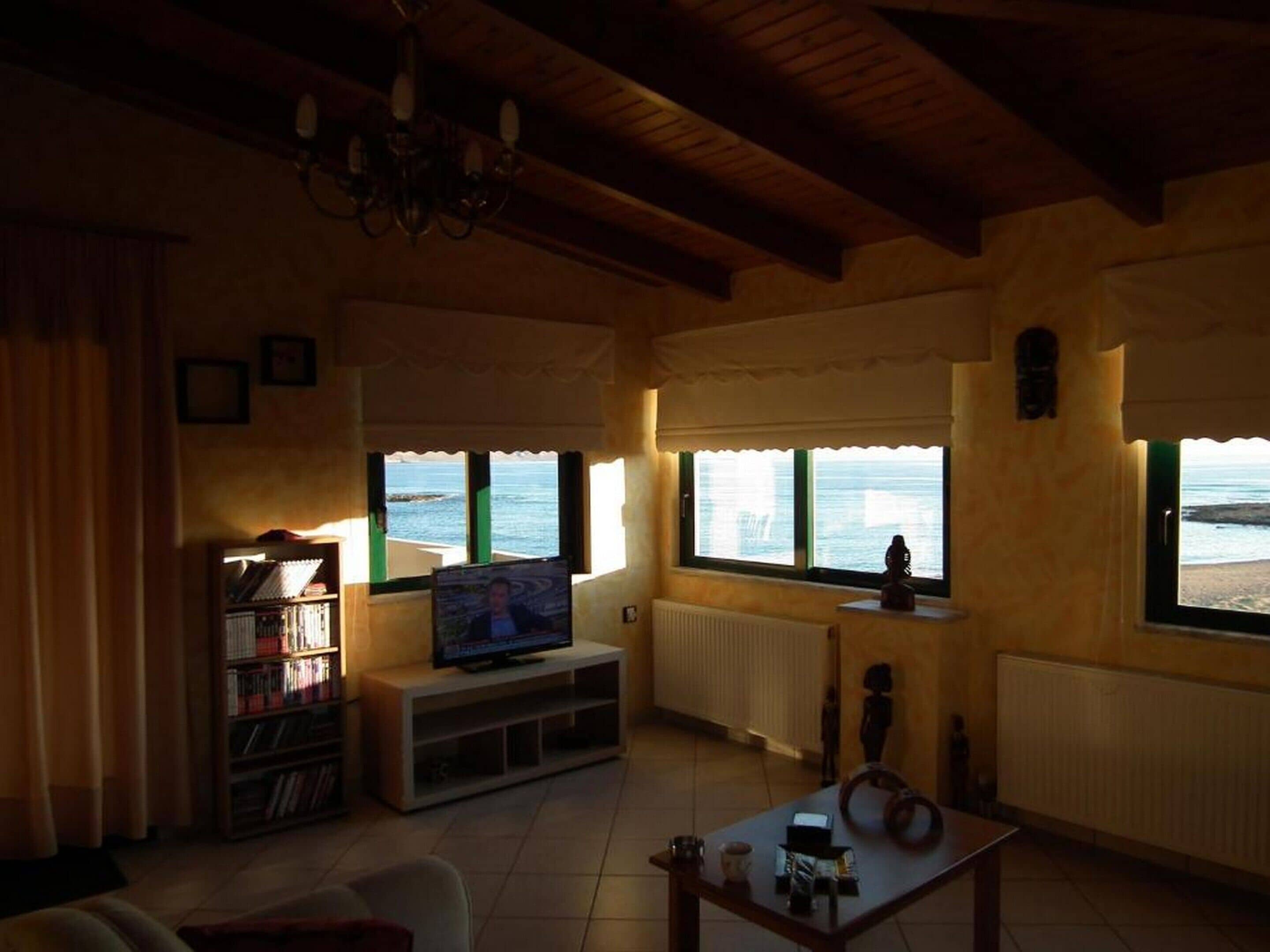 Una sala de estar con televisor, estanterías, una mesa de centro y vista a la playa a través de amplios ventanales.