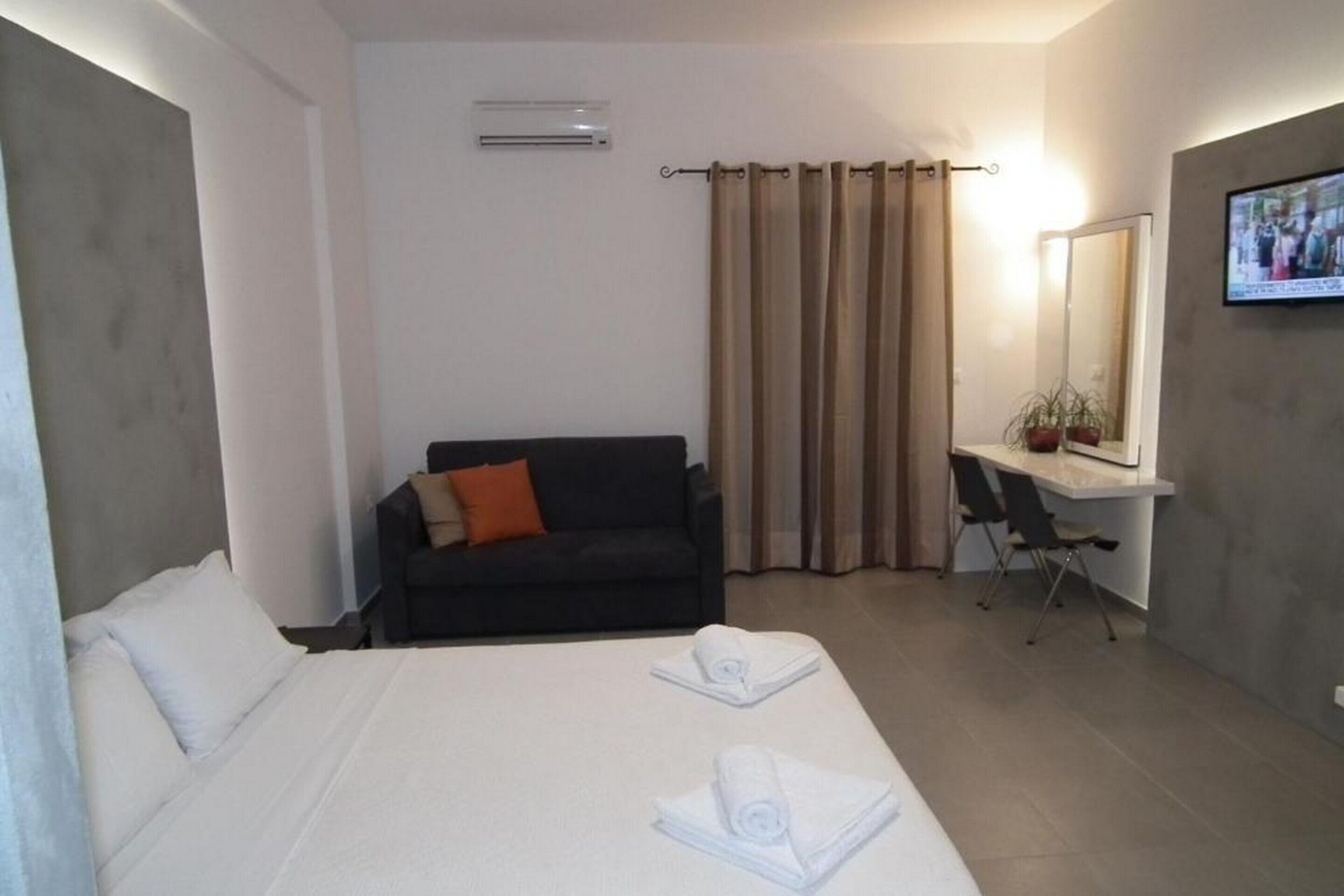A hotel room with a bed, a desk, a chair, a sofa, a TV, and a mirror.
