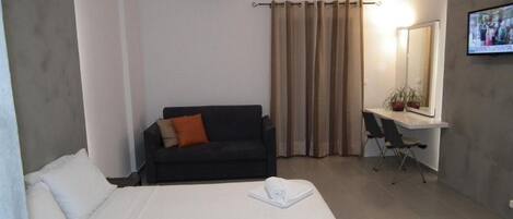 A hotel room with a bed, a desk, a chair, a sofa, a TV, and a mirror.