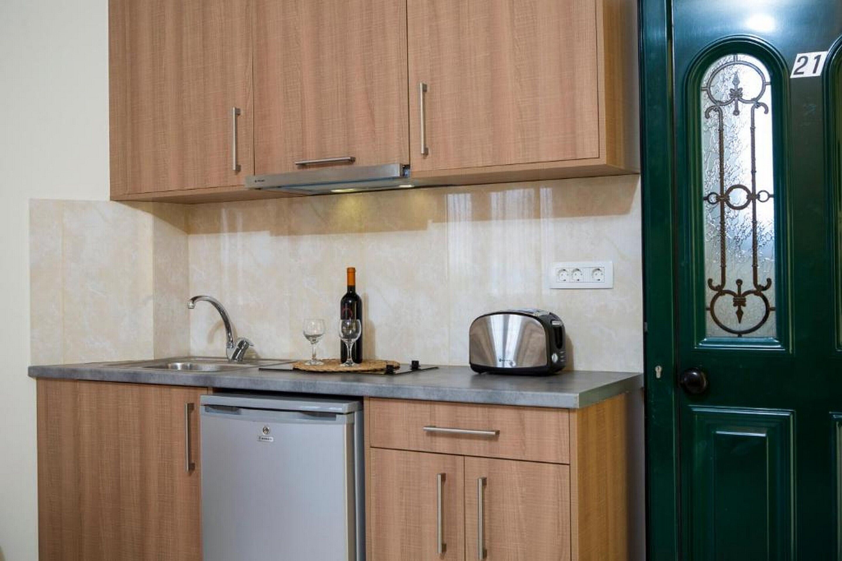 A compact kitchen with wooden cabinets, a built-in dishwasher, a toaster, and a wine glass on the counter.