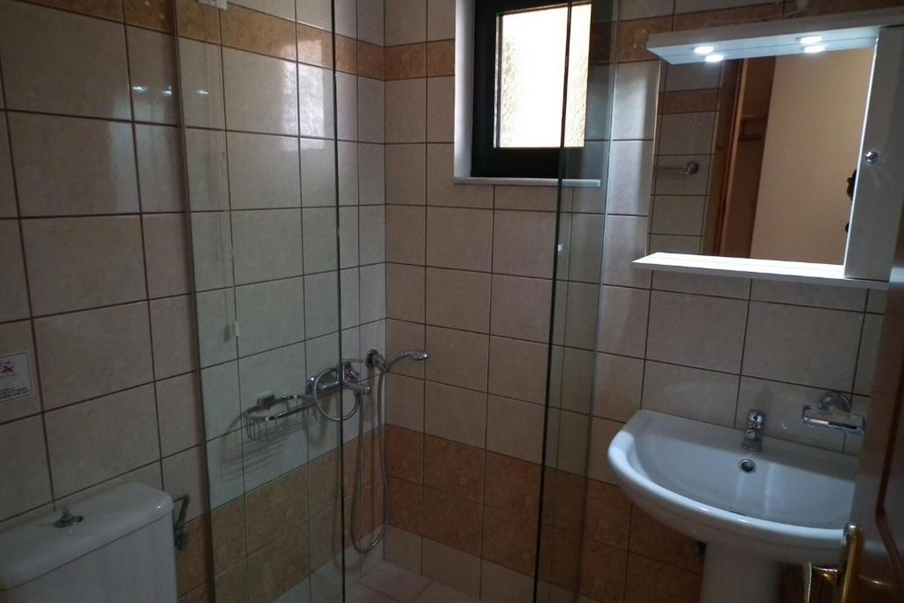 Baño con ducha de vidrio, lavamanos blanco y espejo sobre el lavamanos.