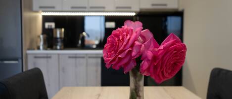 A dining table with a vase of pink flowers and a modern kitchen in the background.