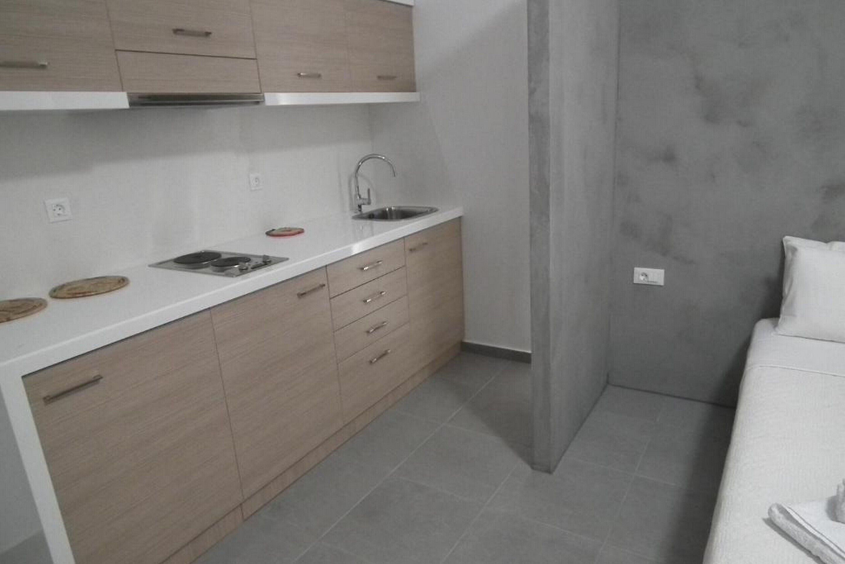 A compact kitchen with a white countertop, a sink, and light wooden cabinets.
