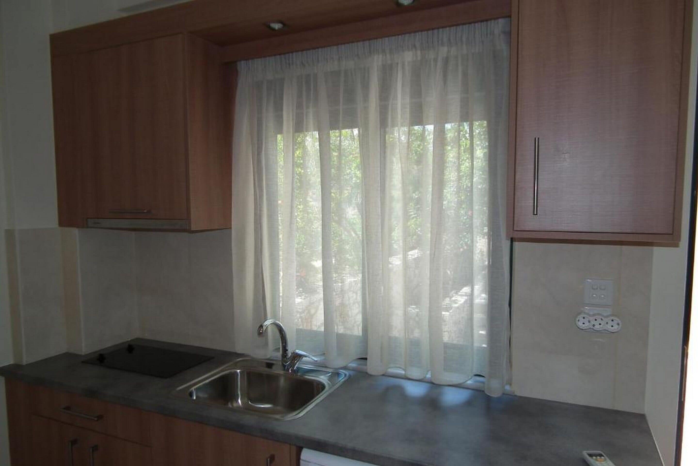A kitchen with wooden cabinets, a stainless steel sink, and a window with sheer curtains.