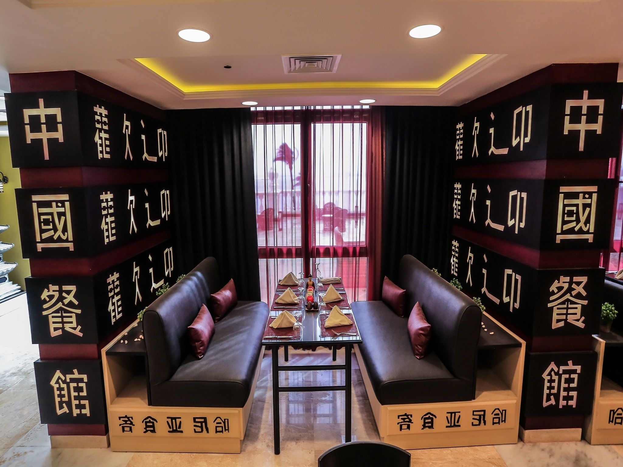 A modern hotel lobby with a central seating area featuring black sofas and a glass-top table. The walls are adorned with vertical black panels displaying Chinese characters.