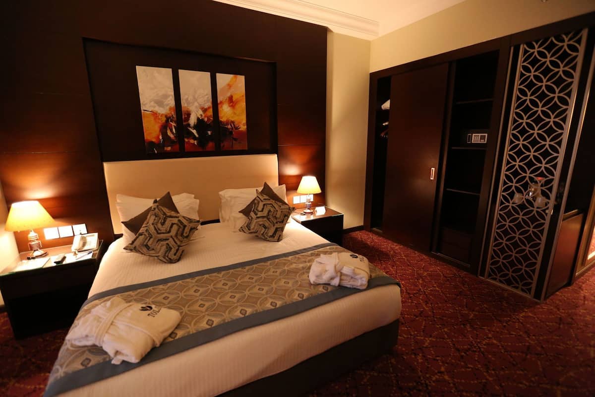 A hotel room with a large bed, two bedside tables with lamps, a painting on the wall, and a wardrobe with a geometric design.
