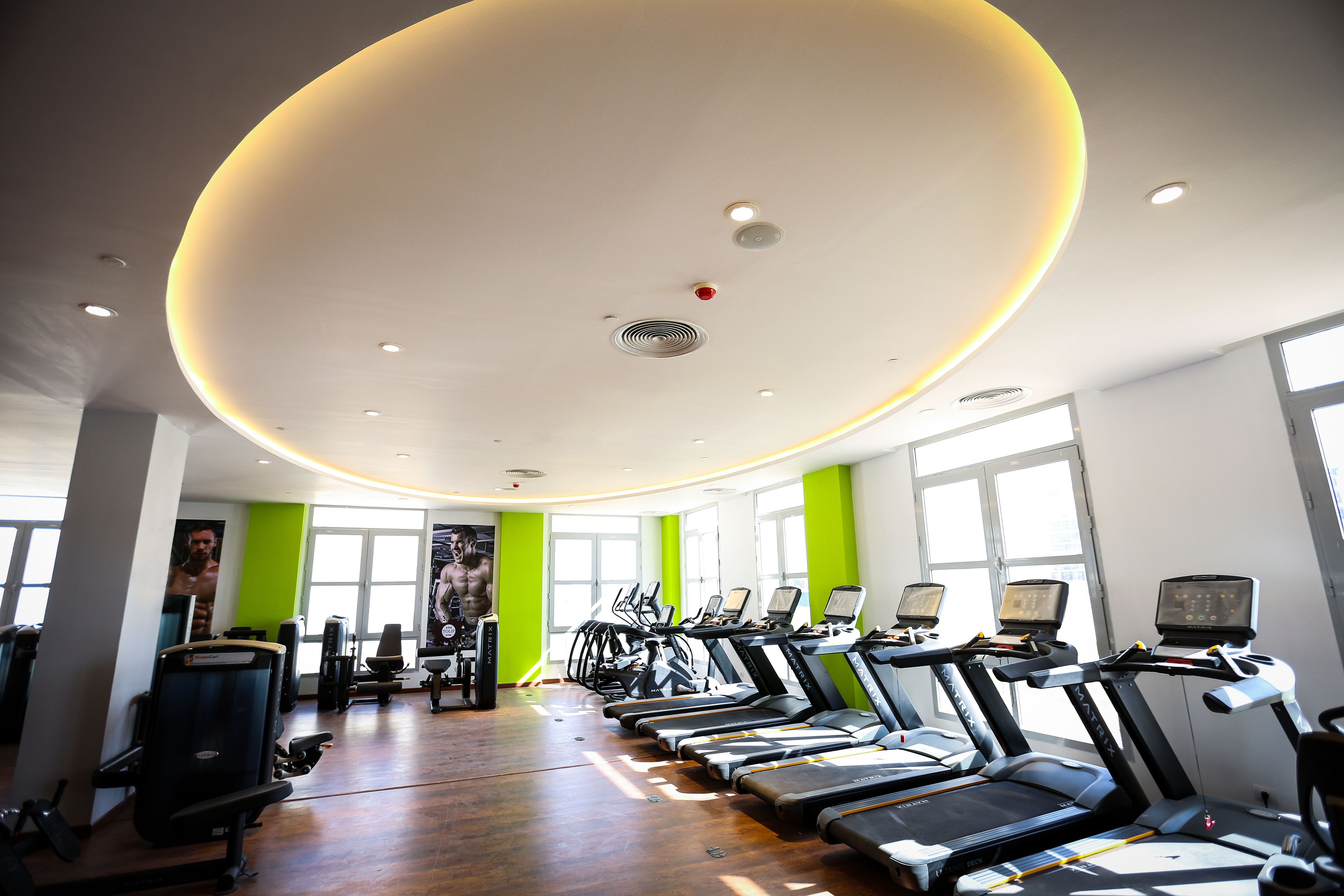 Une salle de sport équipée de tapis de course, d’appareils d’exercice et dotée de grandes fenêtres.