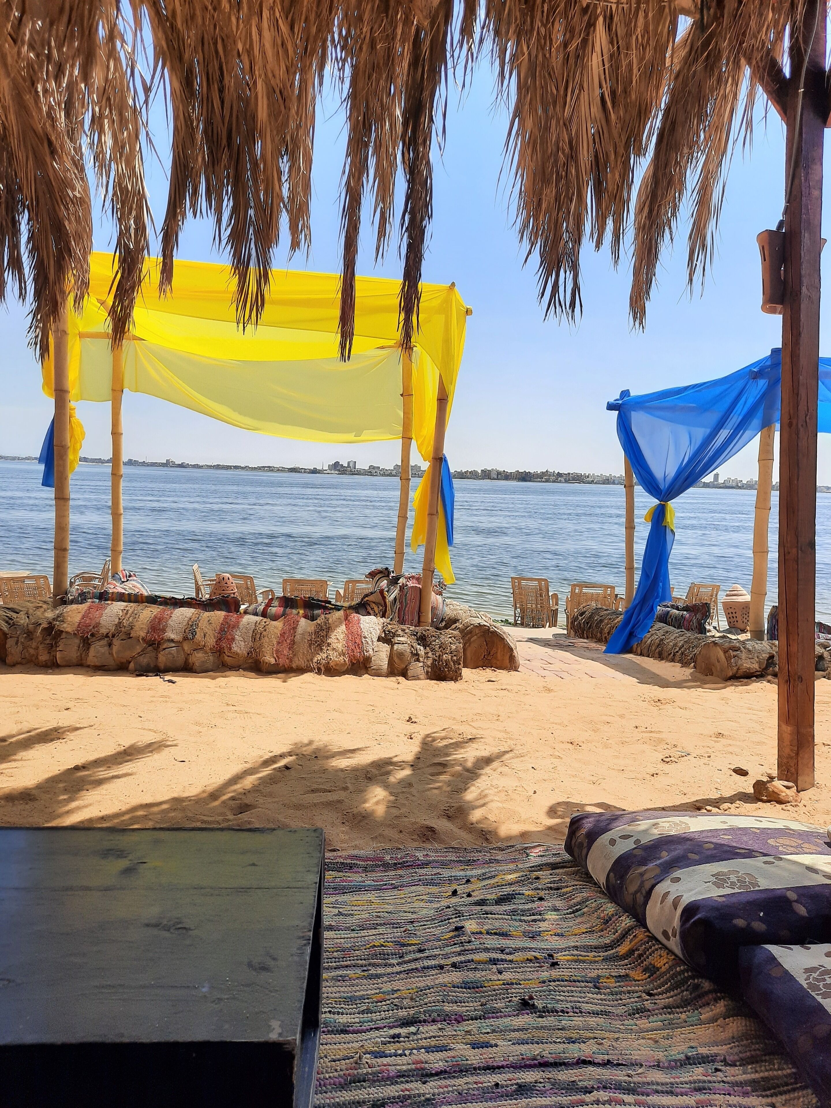 Una playa con una estructura de techo de paja, sillas de madera y un tapete tejido.