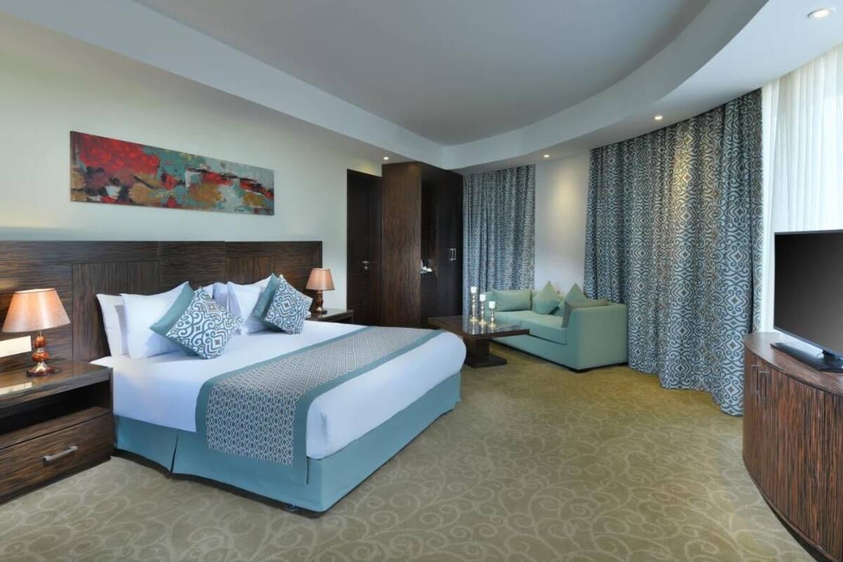 A modern hotel room with a large bed, a sofa, a TV, and a painting on the wall.