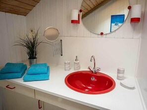 A bathroom with a red sink, white countertop, and a mirror. There are blue towels and a potted plant on the counter. - Juwel Feriendorf - Reihenhaus Sören (Gluecksburg)