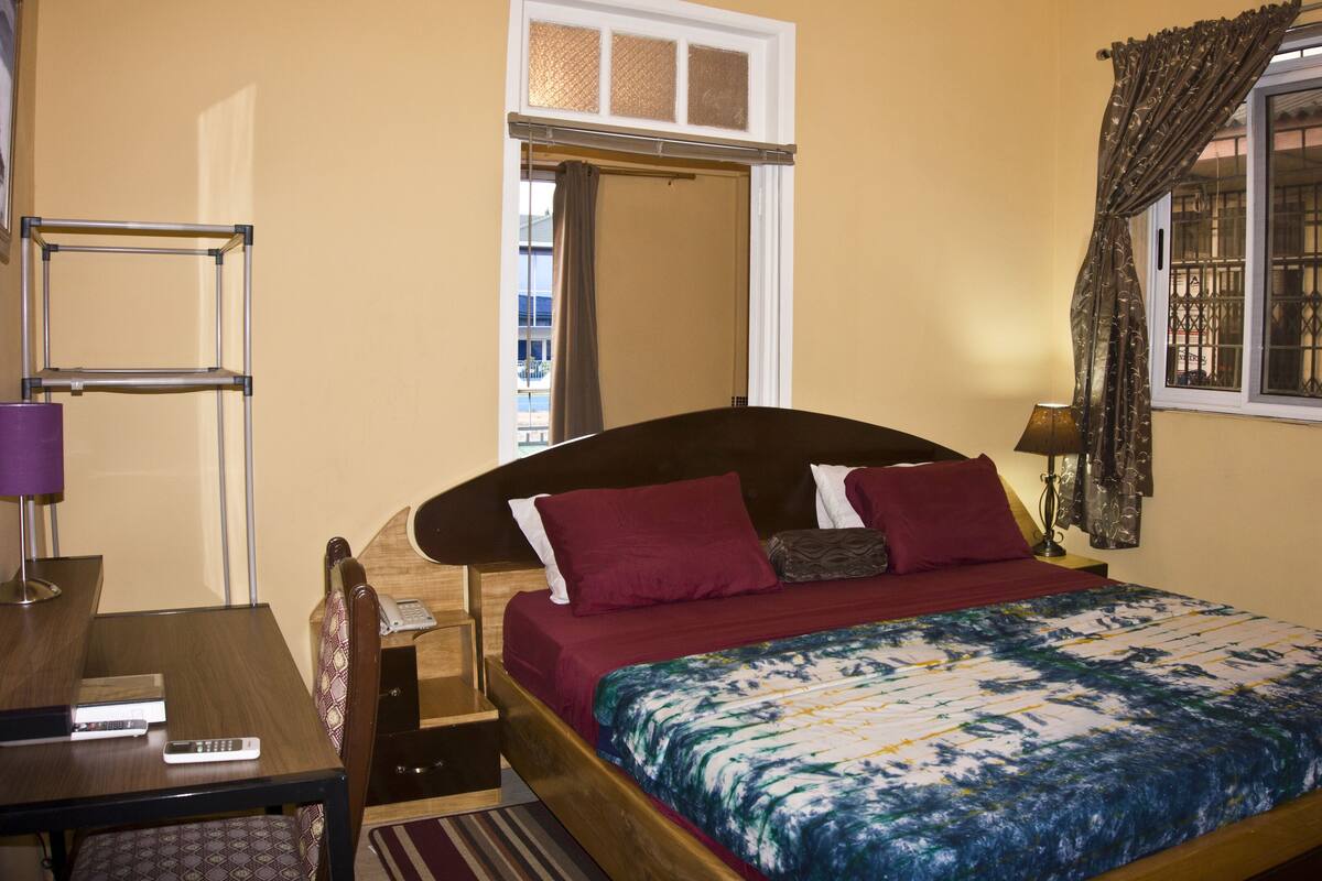 Quarto com cama, escrivaninha, telefone e janela com cortinas.