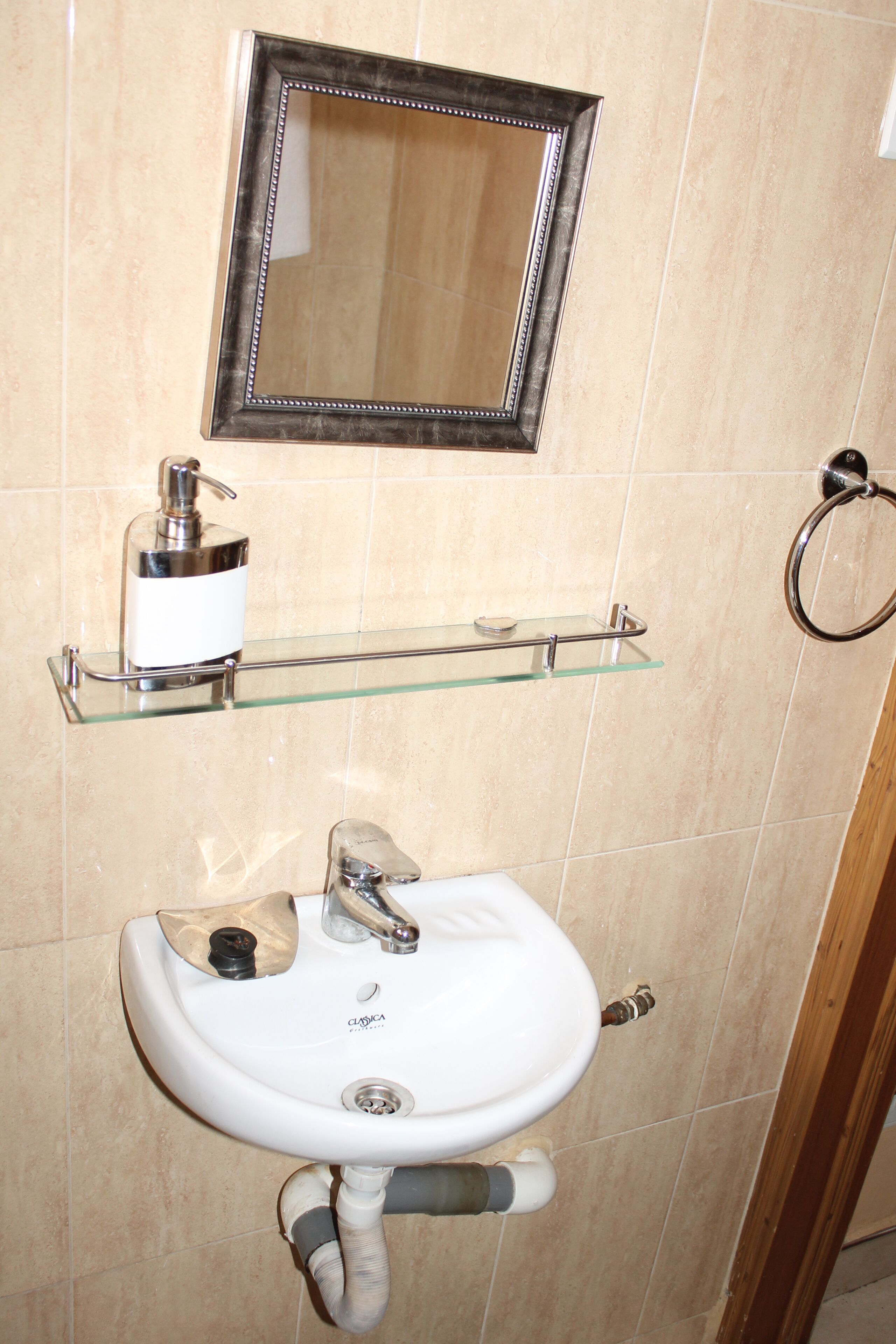 A bathroom with a white sink, a glass shelf with toiletries, a mirror, and a towel rack.