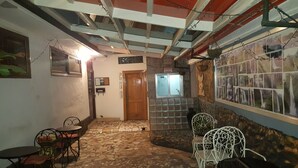 A narrow hallway with a tiled floor, a wooden door, and a wall-mounted information board. There are two metal chairs and a small table with a bowl of fruit. - Jesiwa B's Little Palace (Accra)