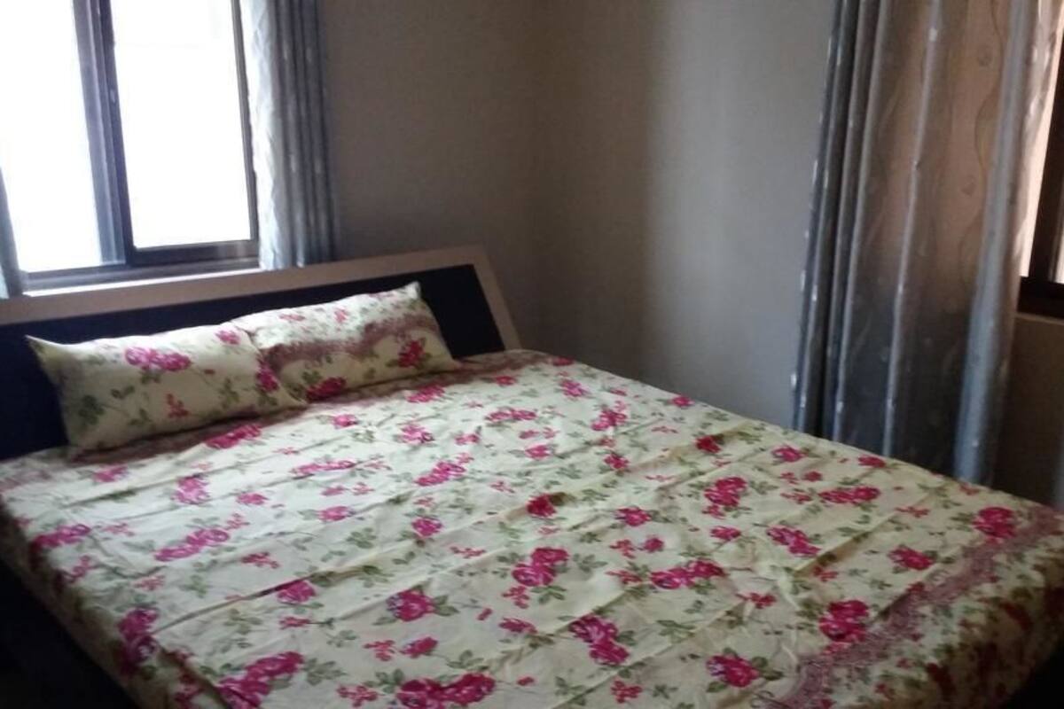 Una cama individual con colcha estampada y almohada a juego en una habitación con ventana y cortinas.