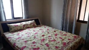 A single bed with a floral bedspread and a matching pillow in a room with a window and curtains.