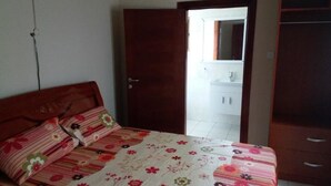 A bedroom with a bed, a wooden door, a wardrobe, and a bathroom visible through the door. - Georgetown Court (Accra)