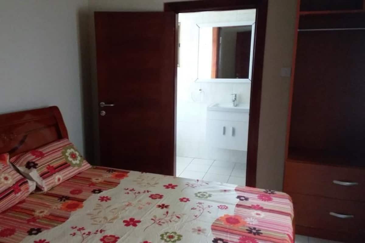 Un dormitorio con una cama, una puerta de madera, un armario y un baño visible a través de la puerta.