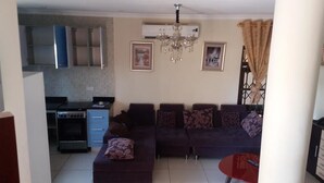 A living room with a sofa set, a dining table, and a kitchen area with cabinets and an oven. - Georgetown Court (Accra)