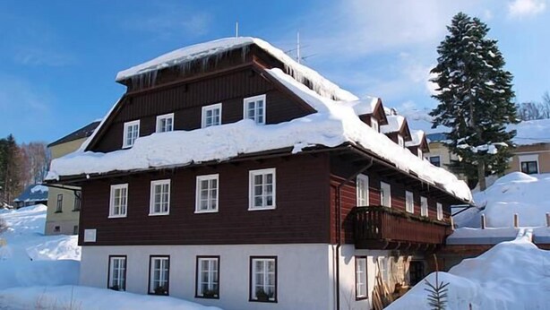 A multi-story wooden building with snow-covered roofs and balconies, surrounded by snow. - Pension Samohel (Rokytnice nad Jizerou)