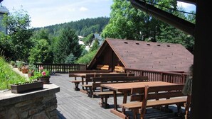 A wooden deck with picnic tables and a stone wall, overlooking a forested area. - Pension Samohel (Rokytnice nad Jizerou)