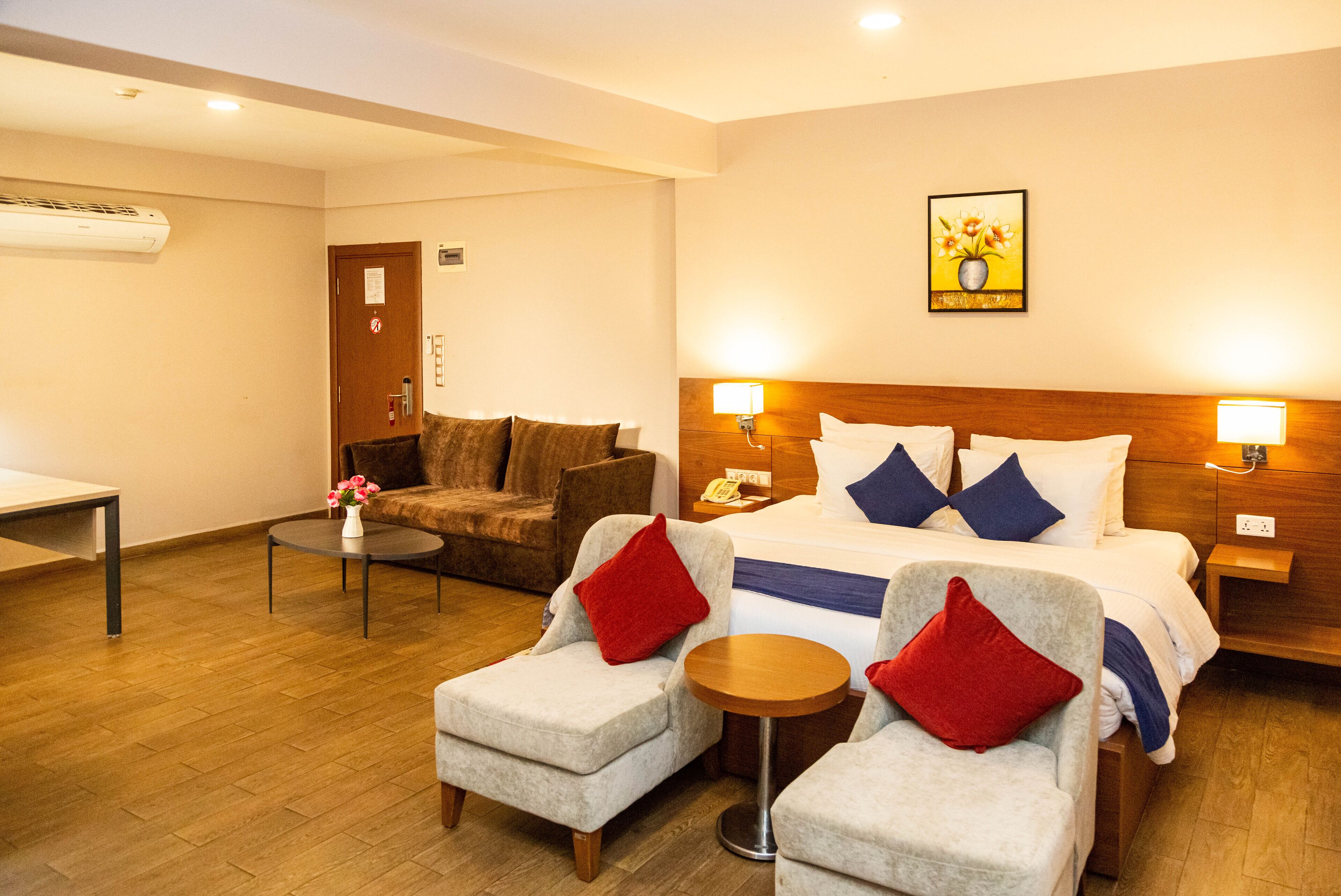 A hotel room with a bed, two armchairs, a small table, a sofa, and a painting on the wall.