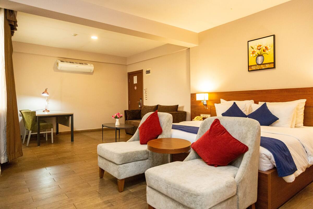A hotel room with a bed, two armchairs, a desk, and a chair.