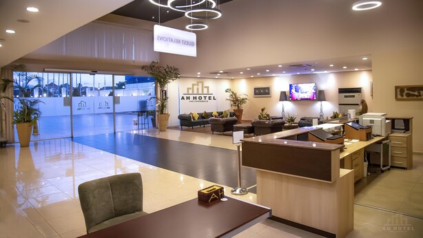 Uma área de recepção de hotel com design moderno, incluindo um balcão de atendimento, espaço para acomodação e uma grande janela com vista para a rua.