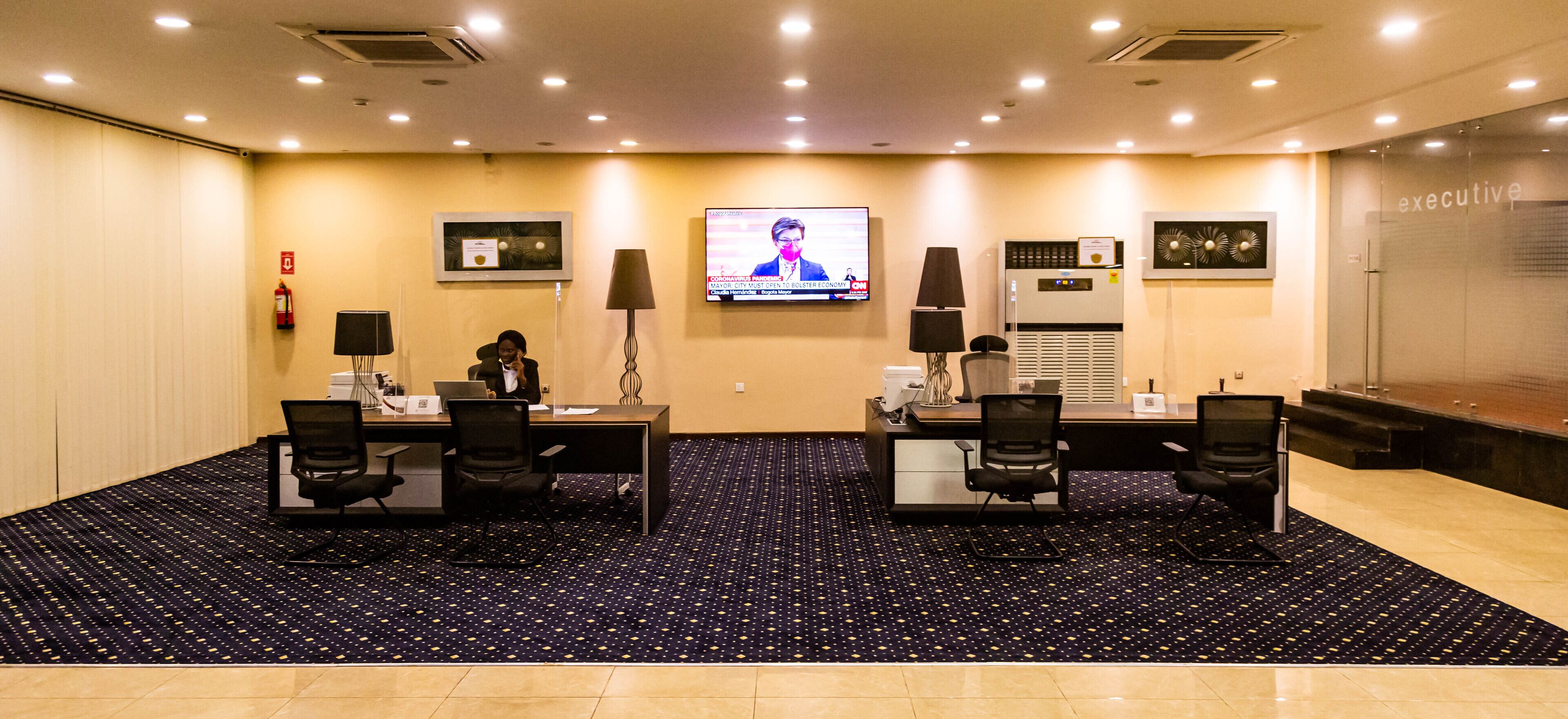 A conference room with a large screen, two desks, chairs, and a fire extinguisher.