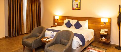 A hotel room with a bed, two armchairs, a nightstand, a lamp, and a painting on the wall.