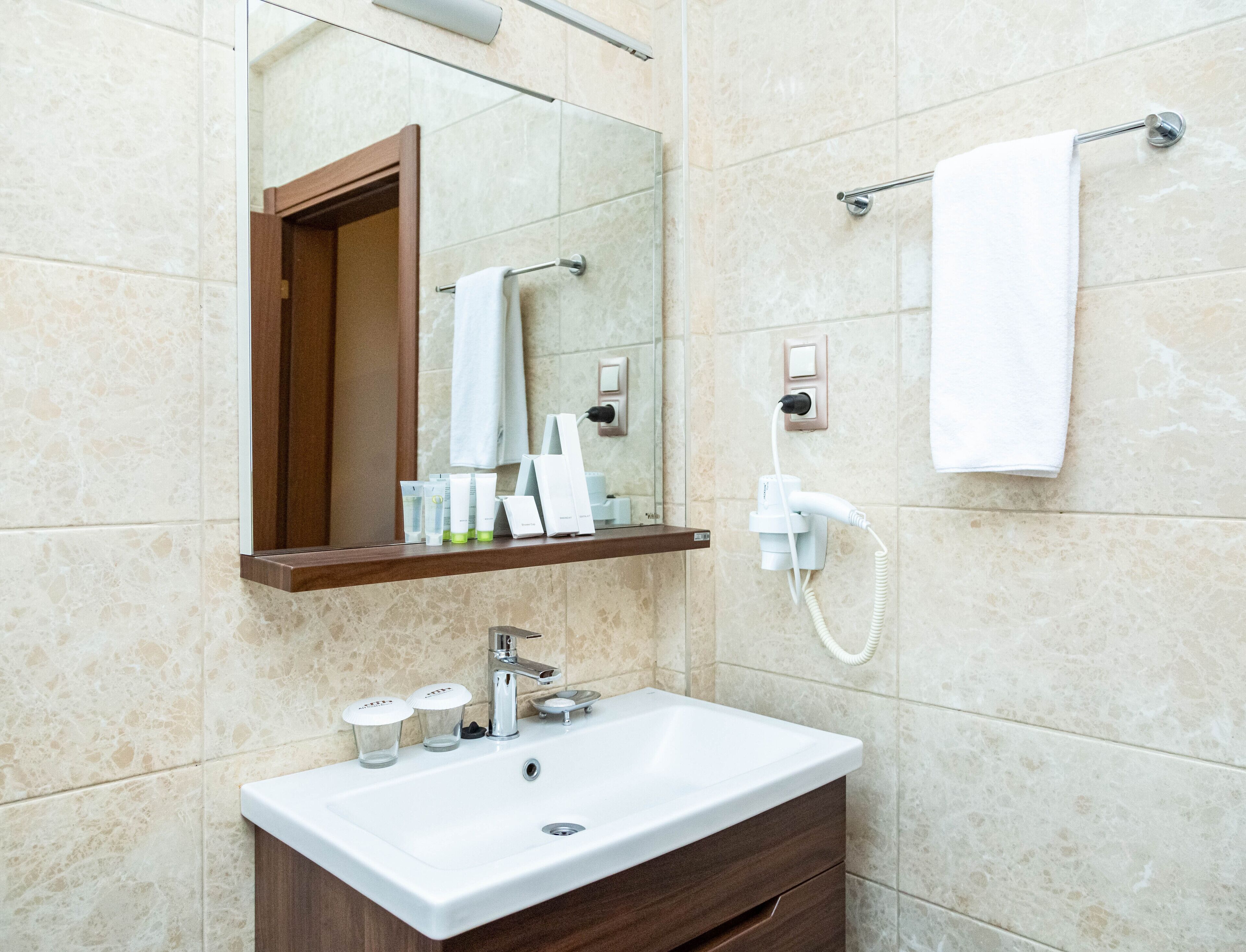Un baño con lavamanos blanco, espejo, toallero y artículos de aseo en una repisa.