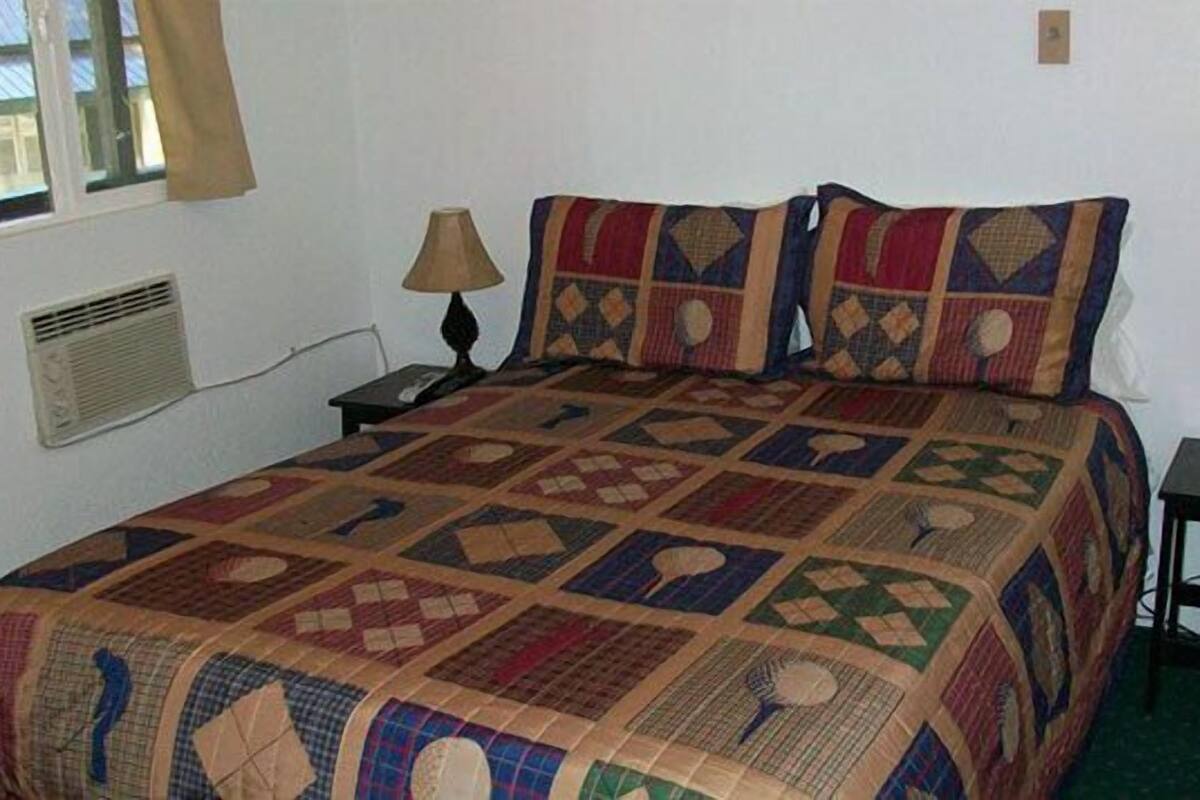 A neatly made bed with a patterned quilt, two bedside lamps, and a small table with a lamp.