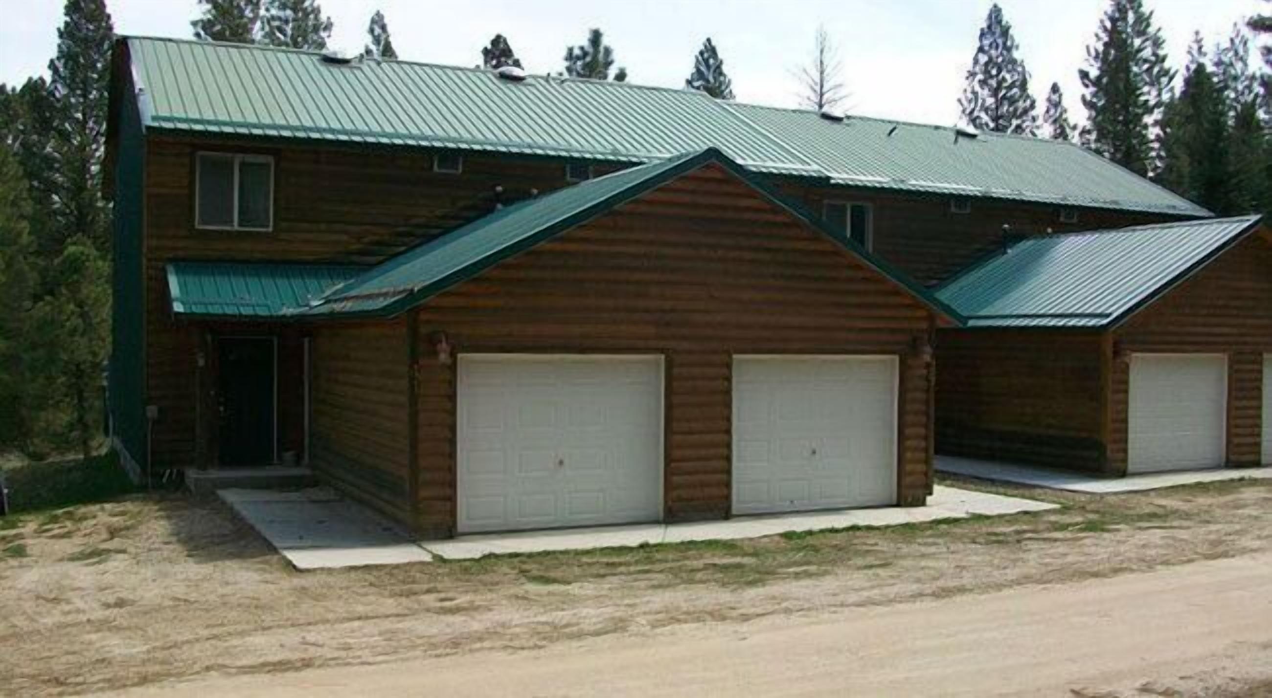 A two-story log cabin with a metal roof and two attached garage doors.