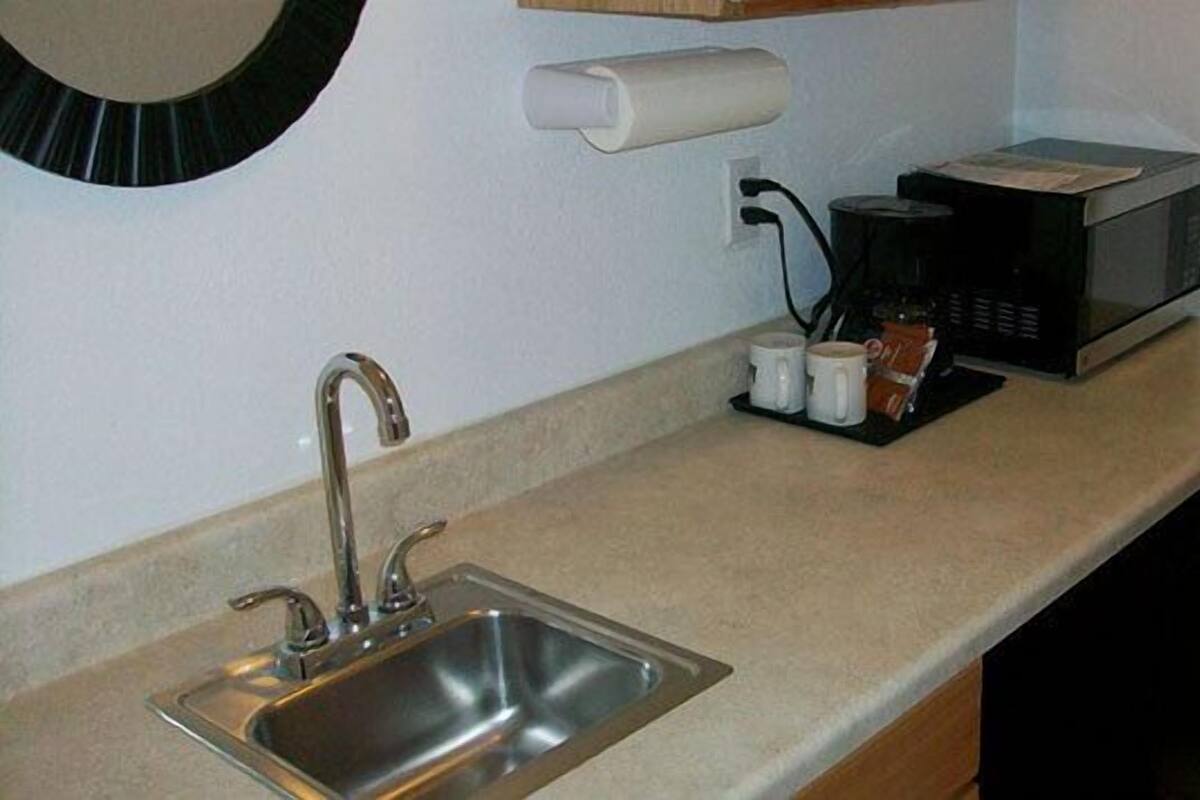 A kitchen with a stainless steel sink, a microwave, and a roll of paper towels on the counter.