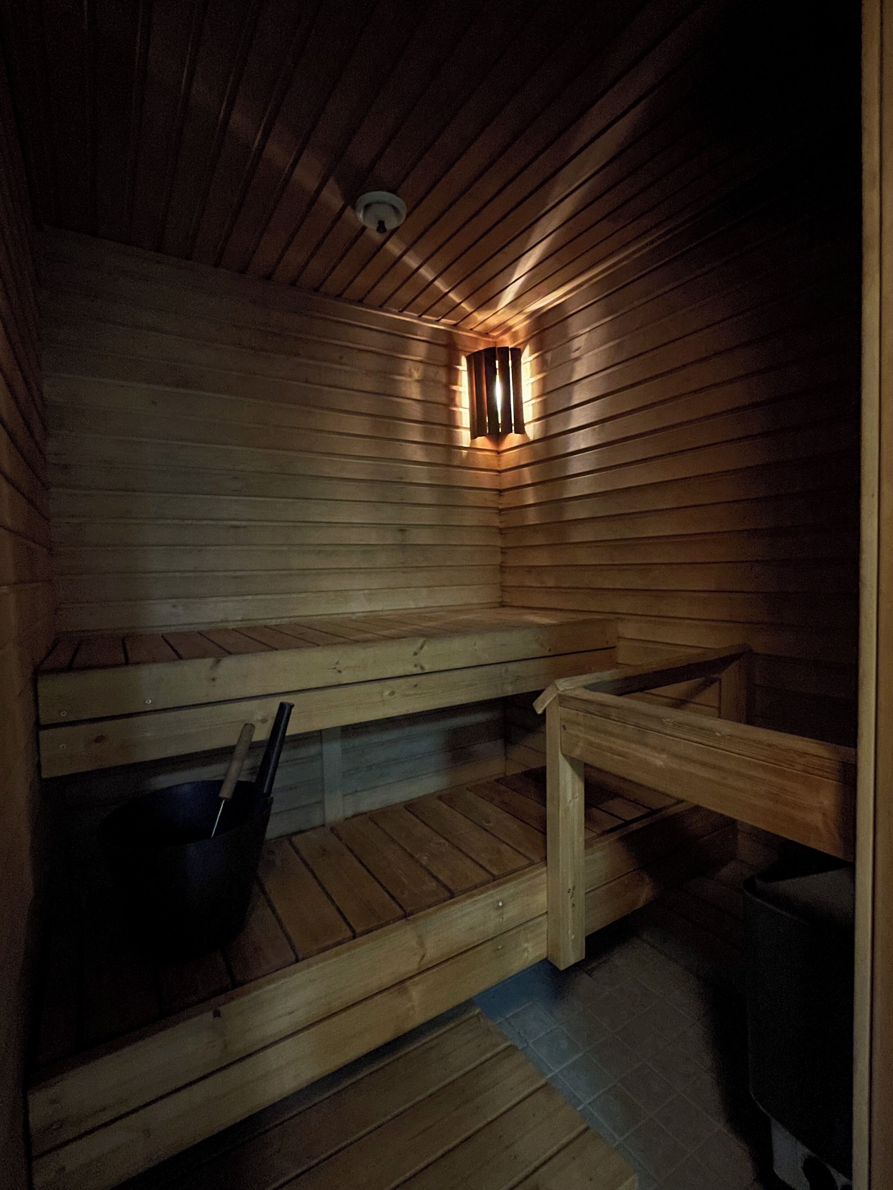 Una sauna con bancos de madera y un cubo negro.