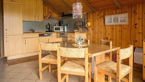 A wooden interior with a kitchen area, including cabinets, a dining table with chairs, and a hanging light fixture. - Ferienwohnung Polly (Gluecksburg)