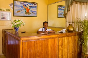 A reception desk with a wooden finish, a vase with flowers, a painting, and a sign that reads "RECEPTION".