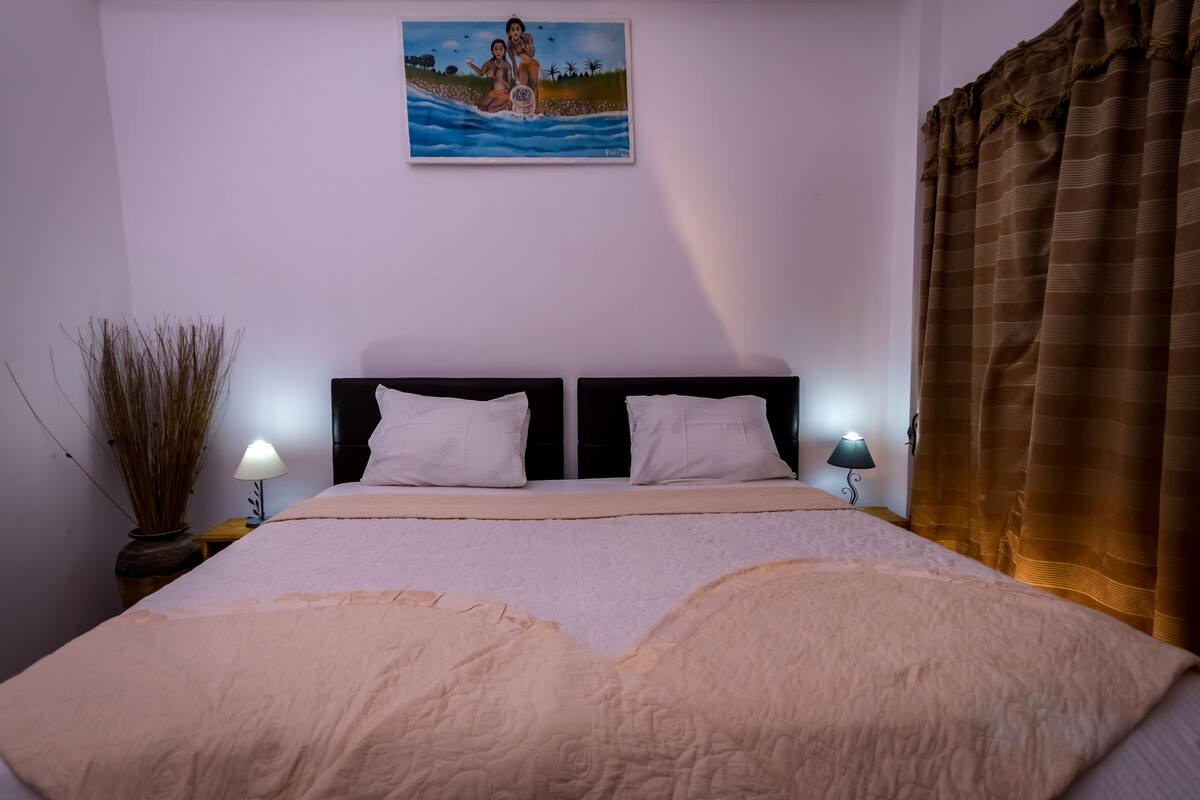 Ein Schlafzimmer mit einem Bett, zwei Nachttischlampen, einem Bild an der Wand und einem Vorhang.