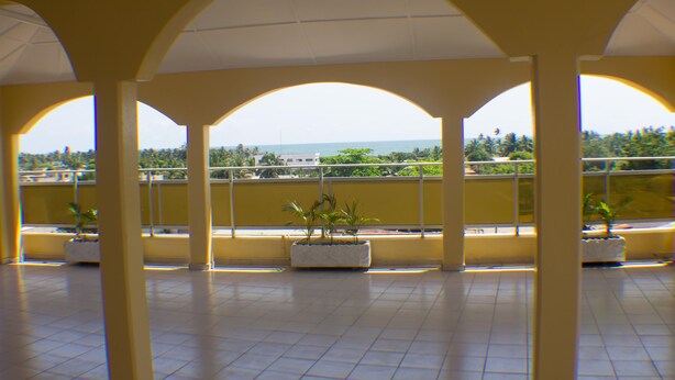 A spacious indoor area with a tiled floor and a view of the sea through arched windows. - Jeane's Appart Hotel (Lomé)