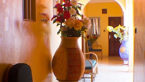 A hallway with a large vase of flowers, a chair, and a door in the background. - Jeane's Appart Hotel (Lomé)