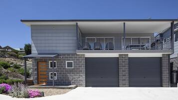 A modern two-story house with a garage, a balcony with chairs, and a stone facade.
