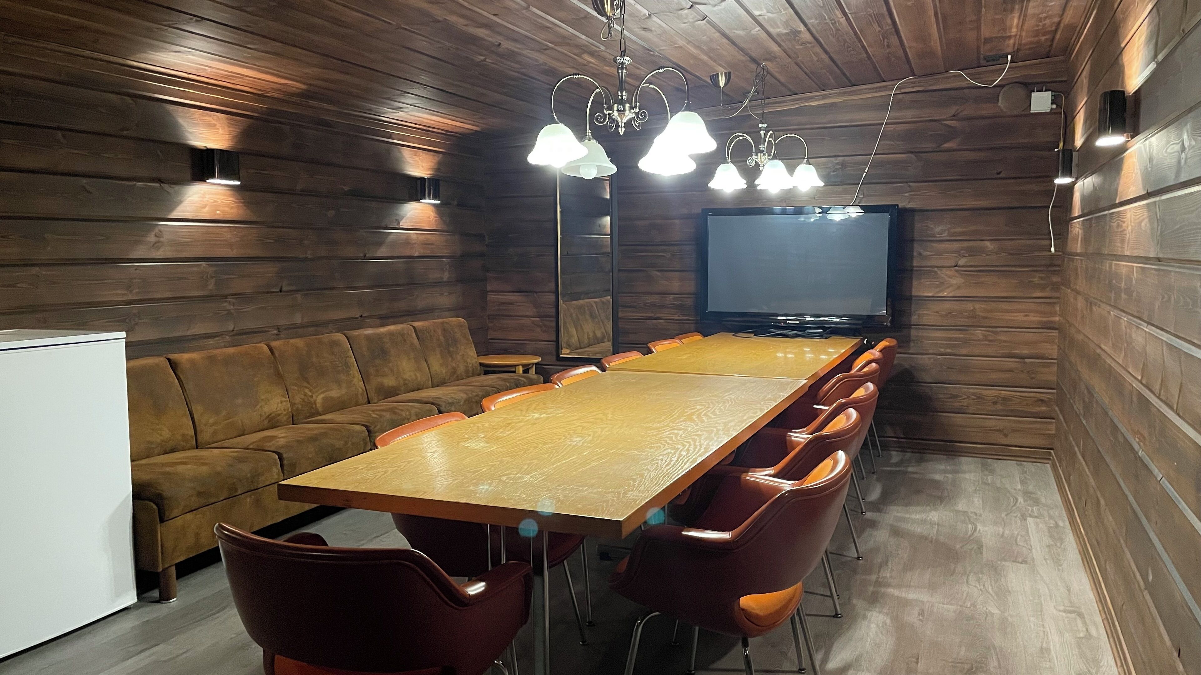 A wooden-paneled room with a long table, several chairs, a sofa, and a television.