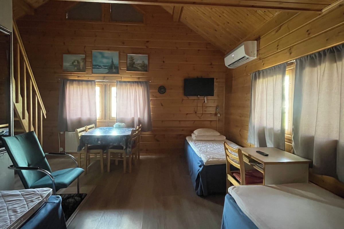 Uma cabana com paredes de madeira, área de jantar com mesa e cadeiras, duas camas e uma televisão fixada na parede.