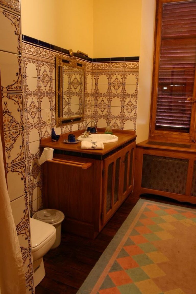 Un baño con baldosas estampadas, un tocador de madera, un inodoro y una ventana con persianas.