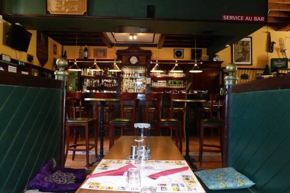 Un espace bar avec des banquettes en bois, un comptoir et une horloge au mur.