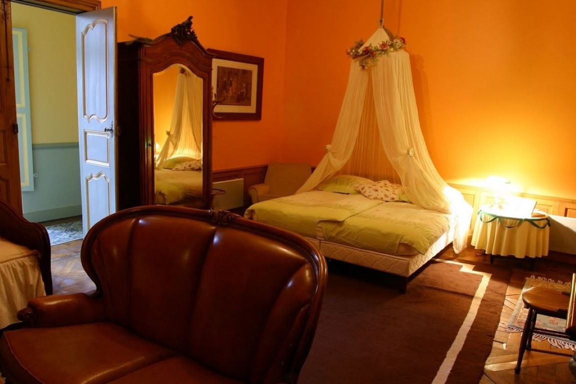 A bedroom with a four-poster bed, a chair, and a bedside table with a lamp.