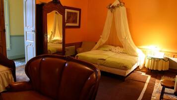 A bedroom with a four-poster bed, a chair, and a bedside table with a lamp.