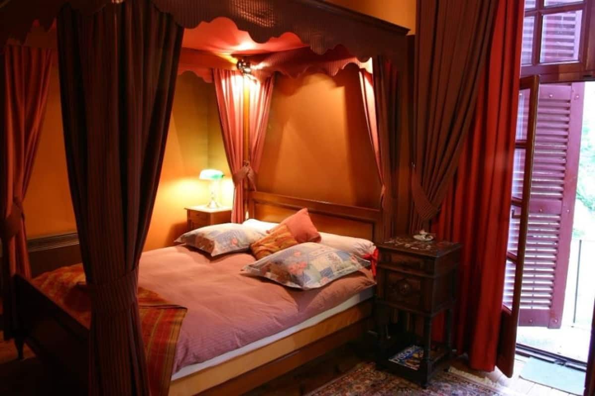 Ein Himmelsbett mit Nachttisch, Lampe und Fenster mit Rollläden.