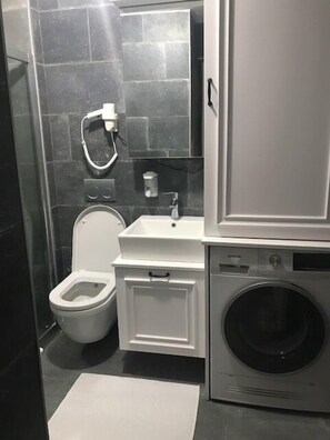 A compact bathroom with a toilet, sink, mirror, and washing machine. - Luxx Suite (Istanbul)