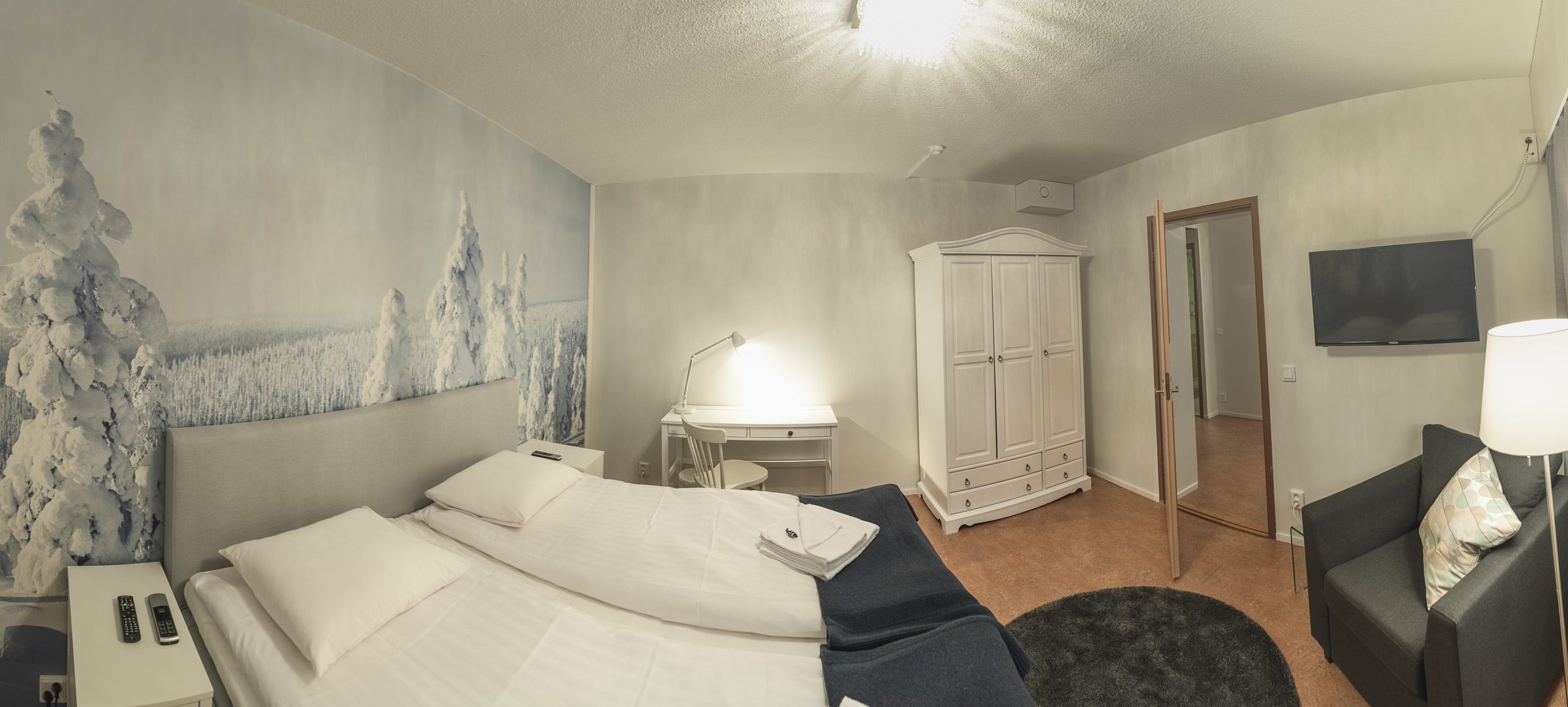 Quarto de hotel com cama, escrivaninha, armário, televisão e sofá.