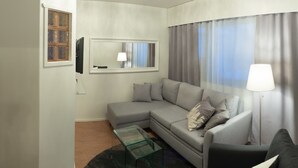 A modern living room with a grey sofa, a glass coffee table, a flat-screen TV mounted on the wall, and a large window with curtains. - Hotelli Kittilä (Kittila)